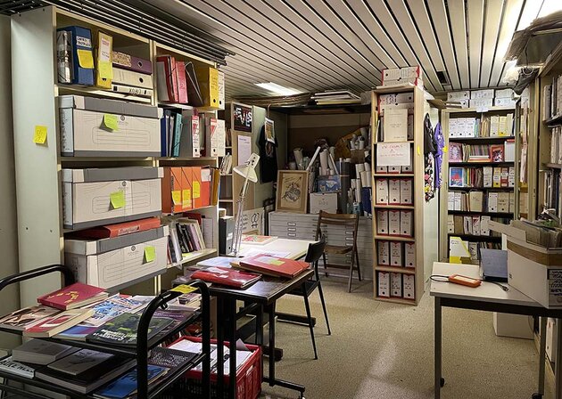 An interior view of the archive in Paris, with book shelves and boxes and loads of material everywhere.