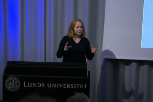 Lovisa Brännstedt, forskare i antikens kultur och samhällsliv vid Lunds universitet, står vid ett podium och föreläser. Hon har axellångt rödblont hår och en svart tröja. 