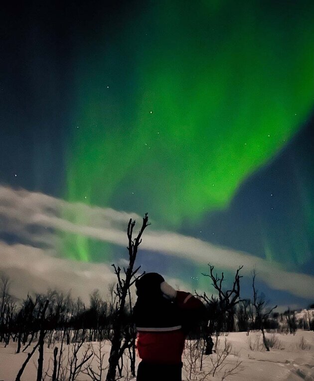 Anna står vinterklädd med ryggen mot kameran. På himlet ett vackert grönt norrsken.