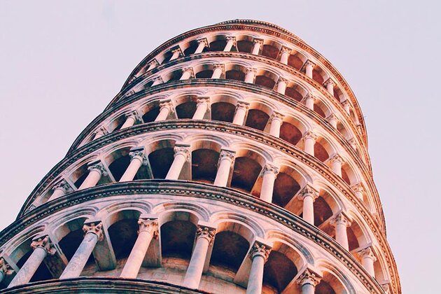 En närbild på det lutande tornet i Pisa, sett nerifrån. En stor del av bilden tas upp av tornets översta våningar med valvbågar uppburna av kolonner.