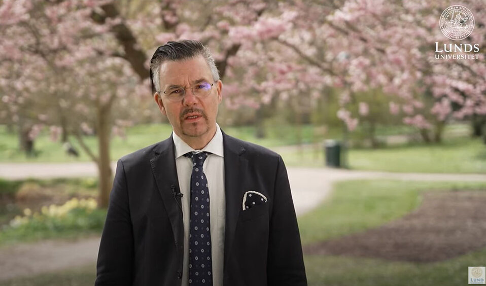 Rektor Erik Renström står framför blommande träd. Han är klädd i kavaj och slips.