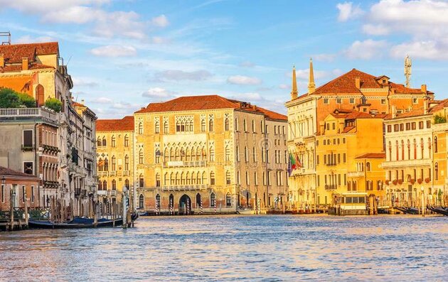 En bred kanal i Venedig med vackra höga byggnader på ömse sidor. Byggnaden rakt fram i bilden är ett flervåningshus med typiska, vackra spetsiga fönsterbågar och med balkonger mot kanalen. Det är huvudbyggnaden för universitetet, Ca’ Foscari University of Venice.