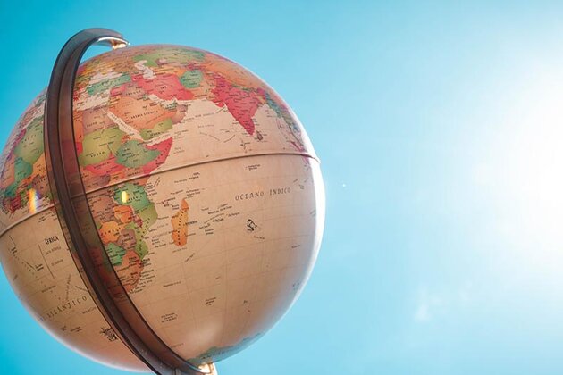 A globe is photographed against a clear blue sky, and it is lit by sun light.