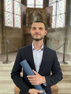 A proud Uladzimir standing with a diploma in his hand.