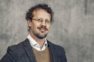 HT-fakulteternas dekan Johannes Persson är fotograferad mot en grå bakgrund. Han har mörkt lockigt hår, kort skägg och mustasch. Håret är uppsatt i en hästsvans. Han bär glasögon, och är klädd i vit skjorta och brun tröja som skymtar under en mörkgrå kavaj.