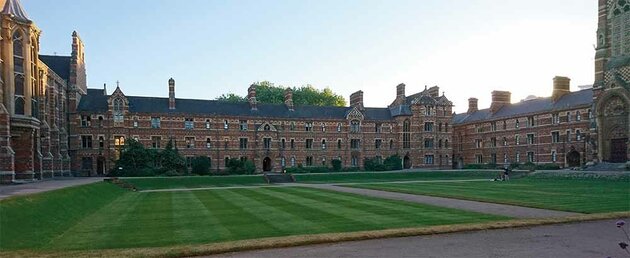 Runt en nedsänkt välklippt gräsmatta finns vackra byggnader i rött tegel. Detta är Keble College i Oxford.