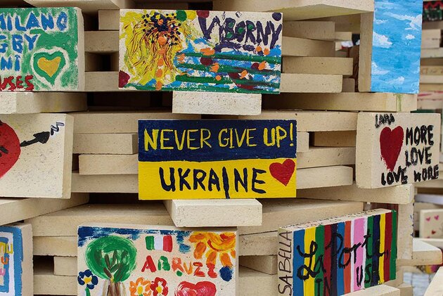 En slags träskulptur bestående av staplade masonitbitar är dekorerad avskyltar med handmålade budskap. På en av skyltarna står det: ”Never give up! Ukraine”.