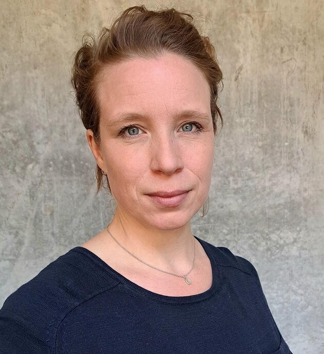 Andrea has short light-coloured hair and blue eyes. She is looking at the camera and smiling a little. She is wearing a black shirt.