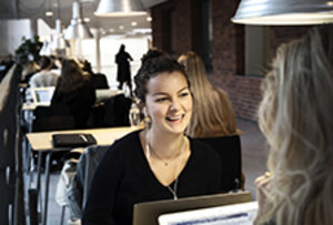 Two female students are working on laptops in a study area.