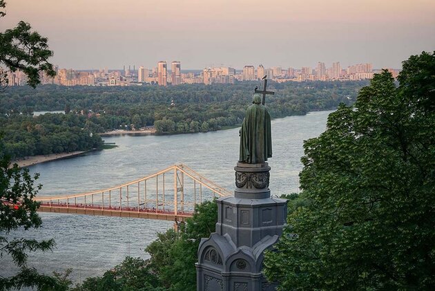 A view of a river in Kiev, with a bronze statue and trees in the foreground.