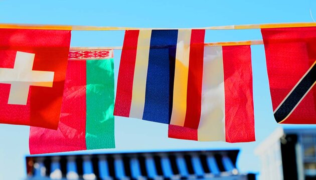 Colourful flags on ropes fluttering quietly in the wind against a clear blue sky. Buildings can be seen in the background.