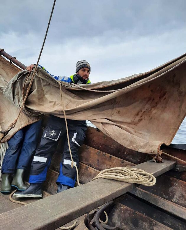 Greer kämpar med ett segel i en träbåt ute på havet.