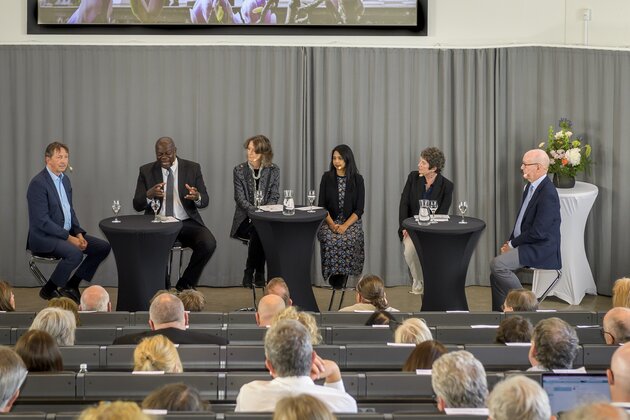 A panel discussion featuring six speakers on a stage in front of an audience