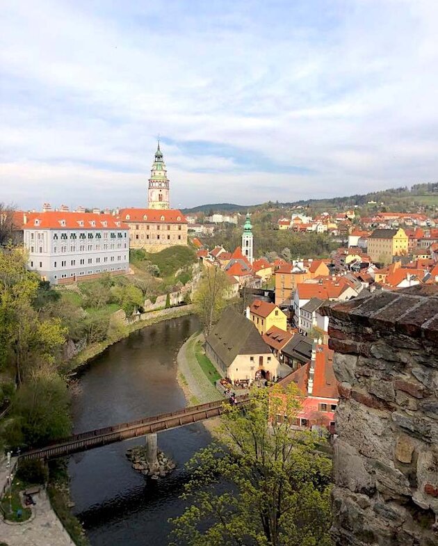Högt uppifrån ser man en flod med en bro över och runt omkring floden en vacker stad med färgglada byggnader, kyrkor och parkområden. Detta är České Budějovice i södra Tjeckien.