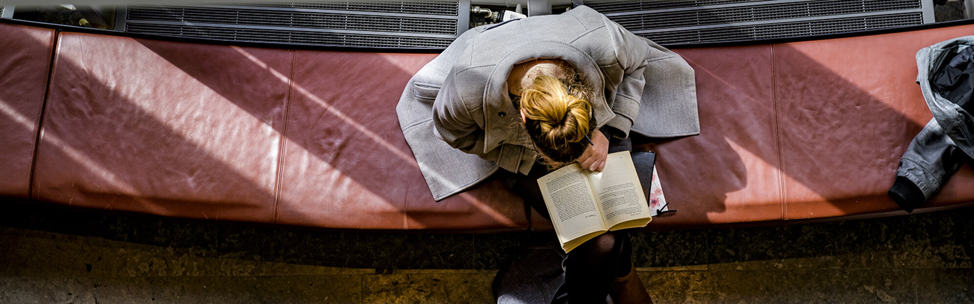 [Translate to English:] Kvinna sitter på en bänk och läser en bok. 