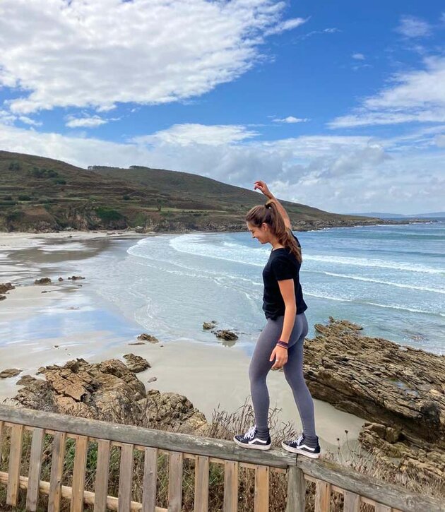 Raquel, dressed in tights and a T-shirt, is balancing on a fence right beside a beautiful beach in norther Spain.