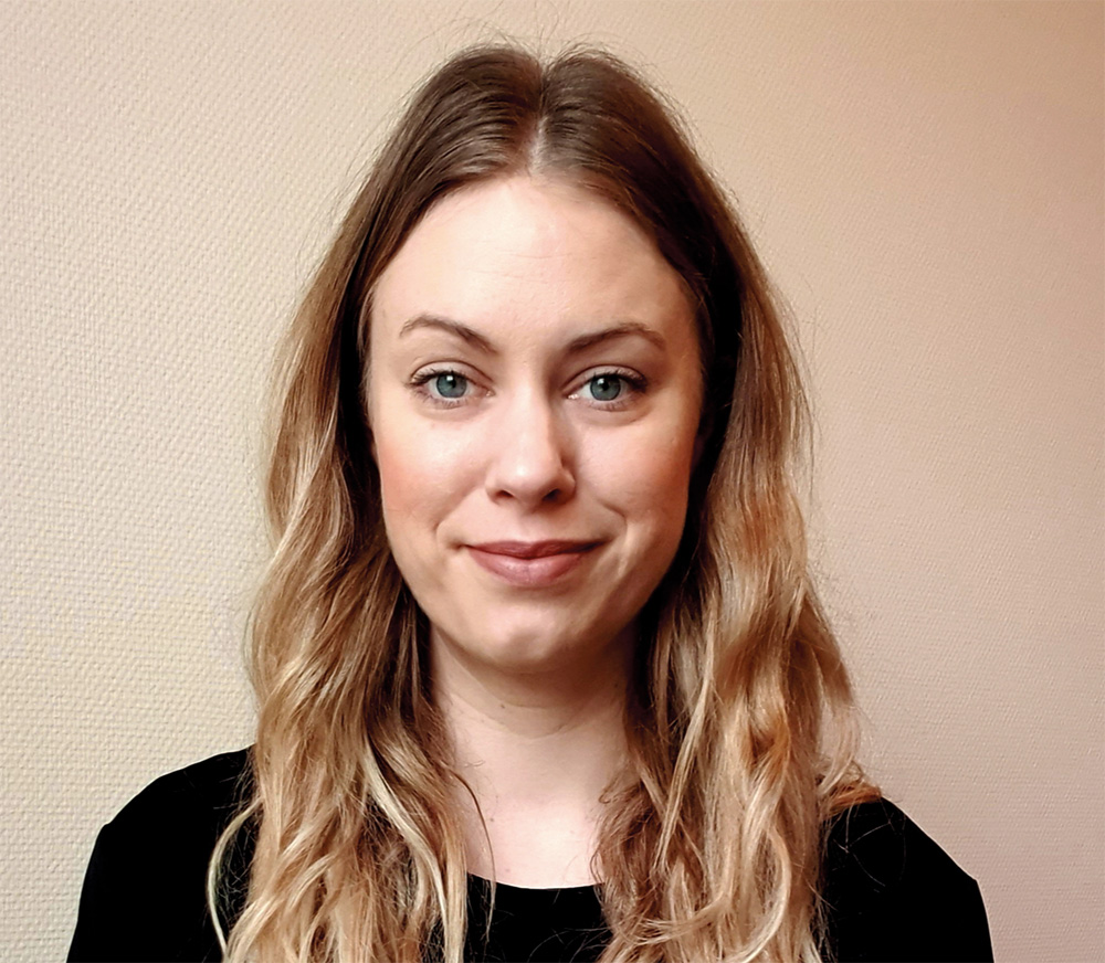 Ellen smiles and looks into the camera. She has long blond har which covers her shoulders. She is dressed in a black sweatshirt.