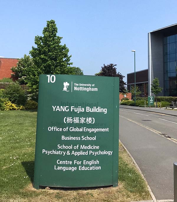 A green sign with white text tells us that next door is the Office of Global Engagement, University of Nottingham. Next to the sign is a paved road and to the right of the road is a glass-fronted building.