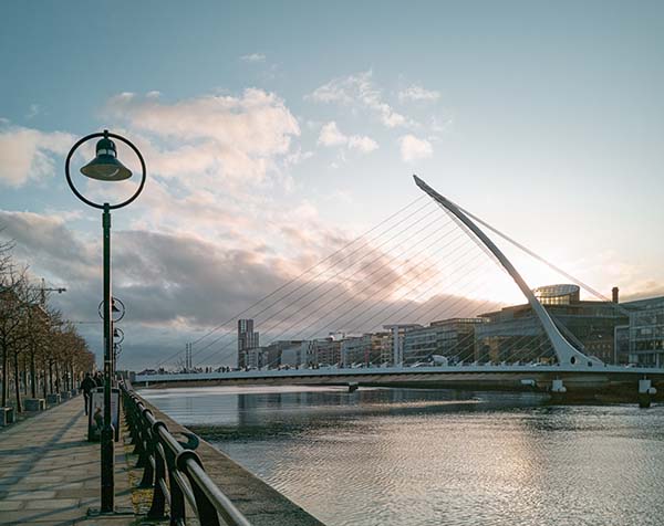 Floden Liffey flyter stilla fram och över den löper den vita, futuristiska Samuel Beckett Bridge. Till vänster i bild finns ett gång- och cykelstråk. Bilden är tagen en tidig morgon i irländska Dublin.