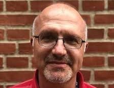  Jordan Zlatev, Kognitiv semiotik, SOL-centrum ALT-text: Jordan står framför en röd tegelvägg och tittar rakt in i kameran. Han har svarta stålbågade glasögon och en röd pikétröja. Han har kort hår, kort skägg och mustasch.